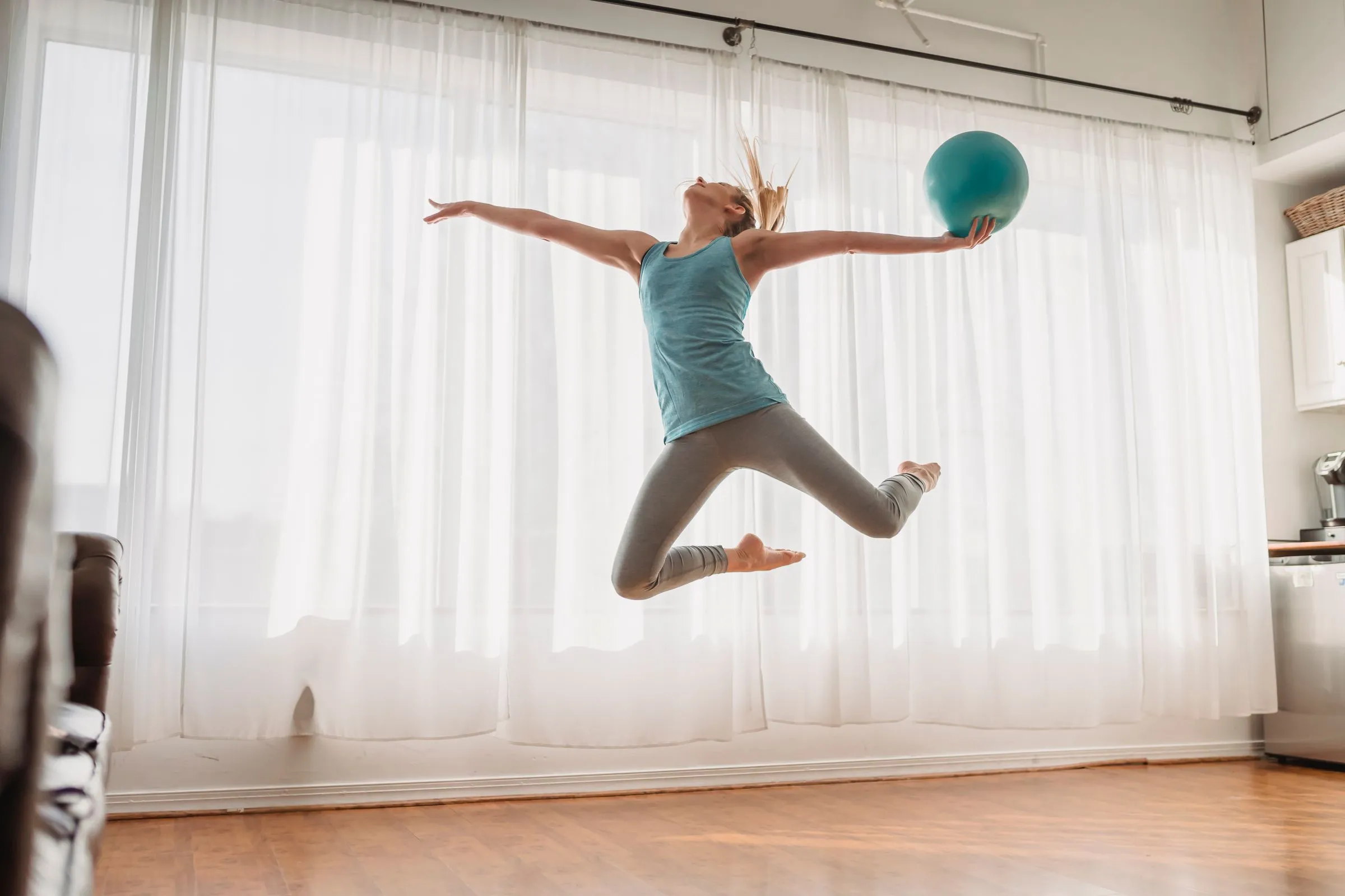 Dona amb pilota de pilates en un moviment dinàmic davant de cortines clares